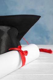 Photo of Graduation hat and student's diploma on white wooden table, closeup