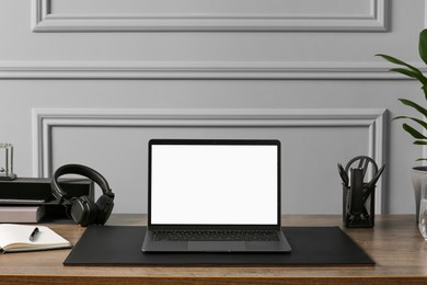 Stylish workplace with laptop, houseplant and stationery on wooden table near light grey wall