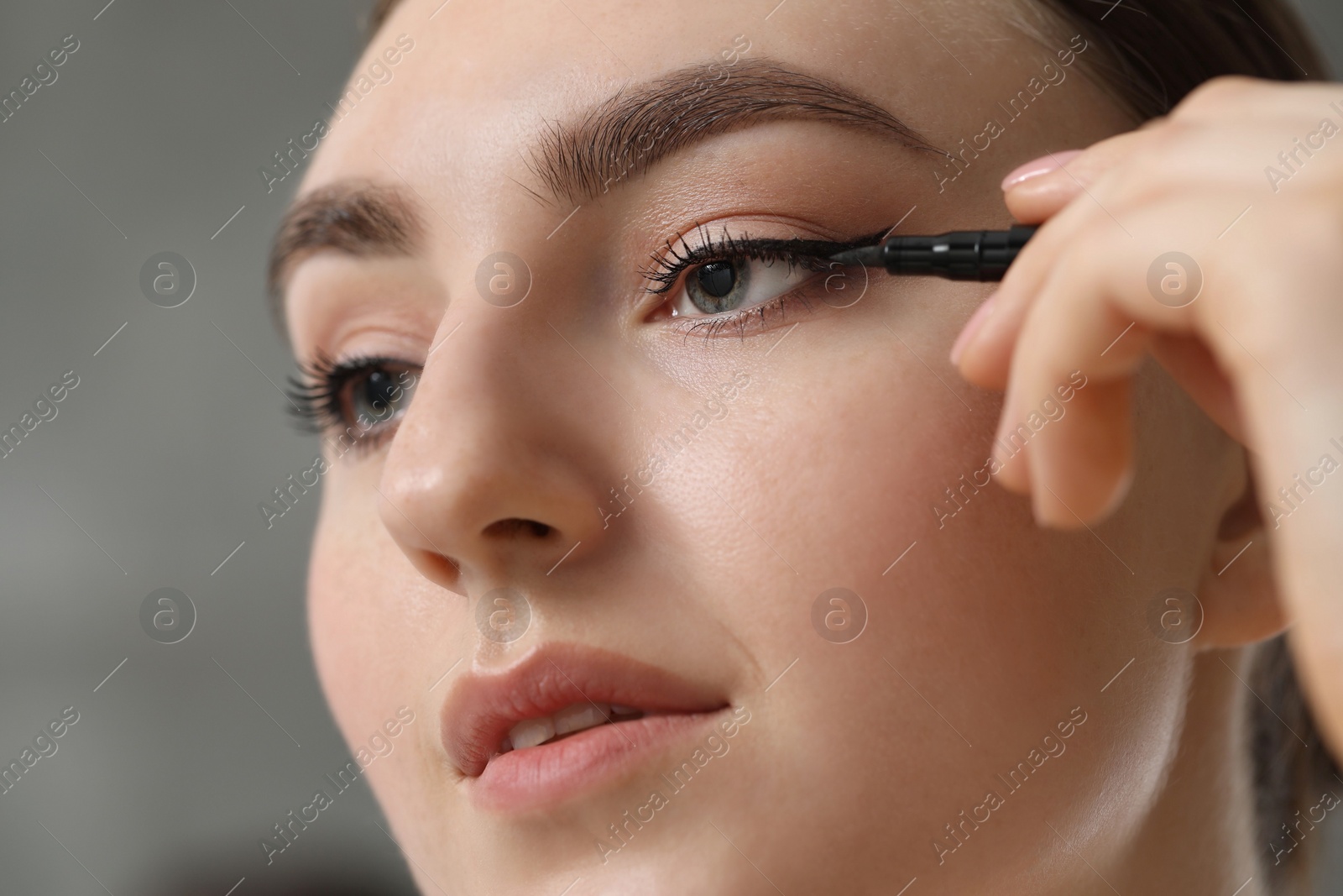 Photo of Makeup product. Woman applying black eyeliner on blurred background, closeup