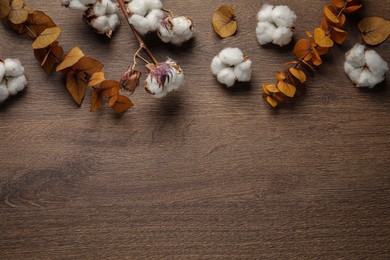 Photo of Dry cotton branch with fluffy flowers and yellow leaves on wooden table, flat lay. Space for text