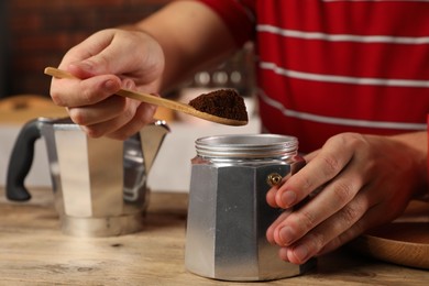 Photo of Man putting ground coffee into moka pot at wooden table indoors, closeup