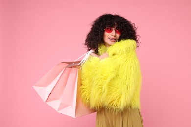 Happy young woman with shopping bags on pink background