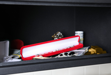 Photo of Open black steel safe with money, gold bars and jewelry on shelf, closeup