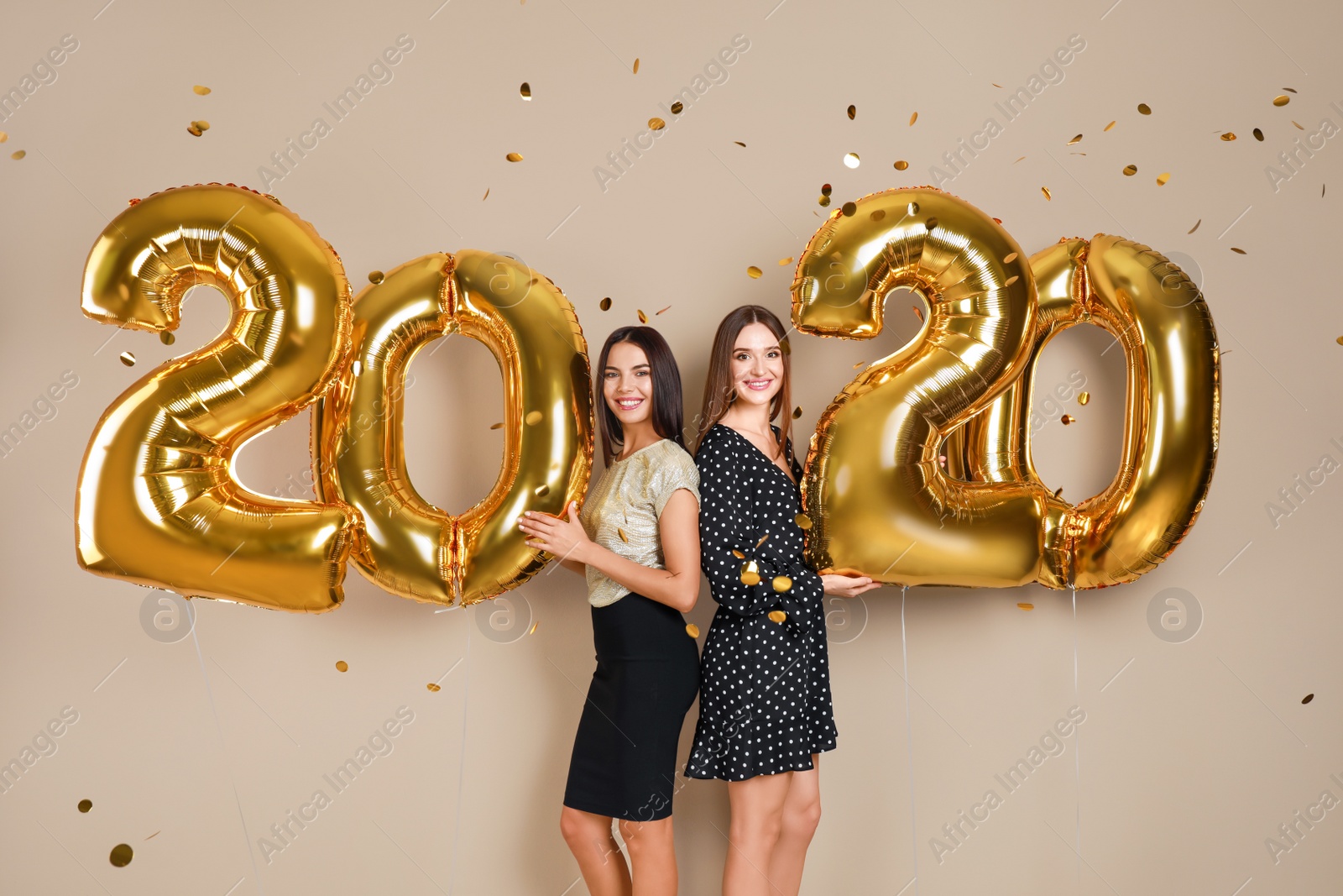 Photo of Happy young women with golden 2020 balloons on beige background. New Year celebration