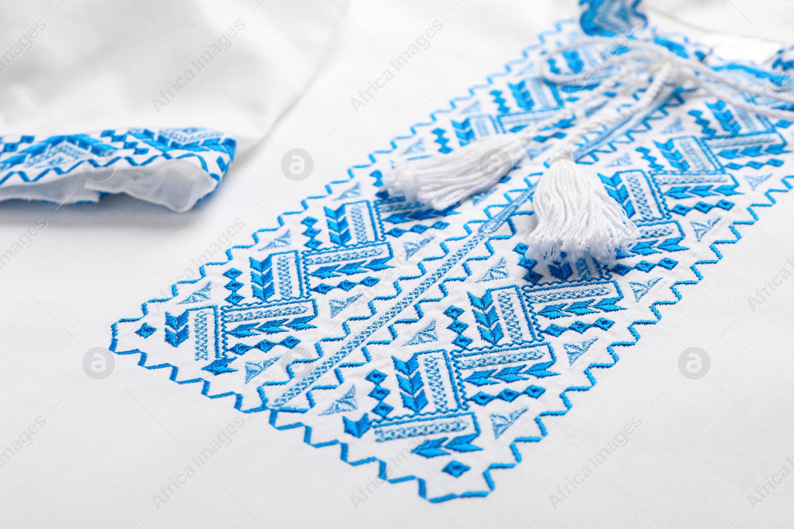 Photo of Beautiful white shirt with light blue Ukrainian national embroidery, closeup