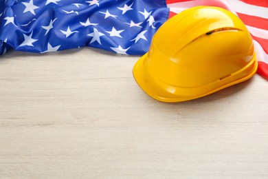 Photo of Yellow protective hard hat and American flag on white wooden table. Space for text