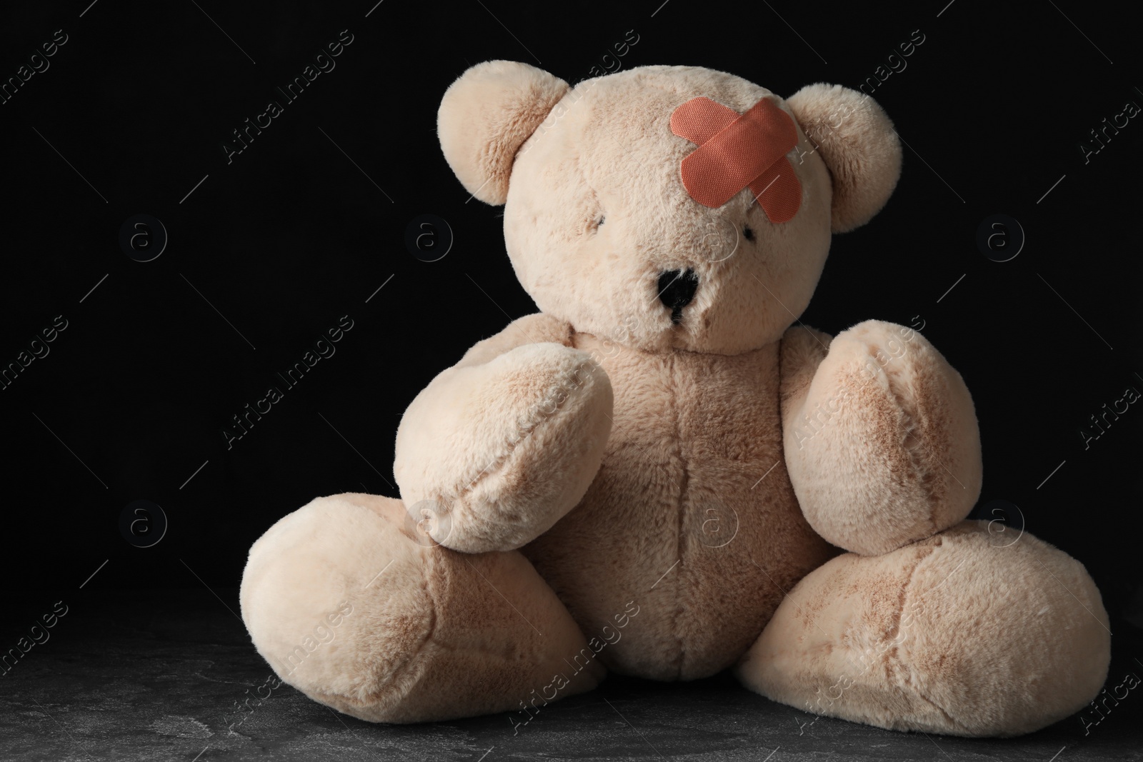 Photo of Toy Teddy bear with sticking plasters on grey stone table