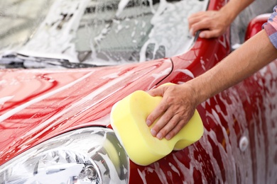 Man washing red auto with sponge at car wash, closeup