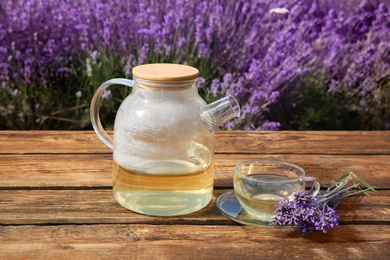 Photo of Tasty herbal tea and fresh lavender flowers on wooden table in field