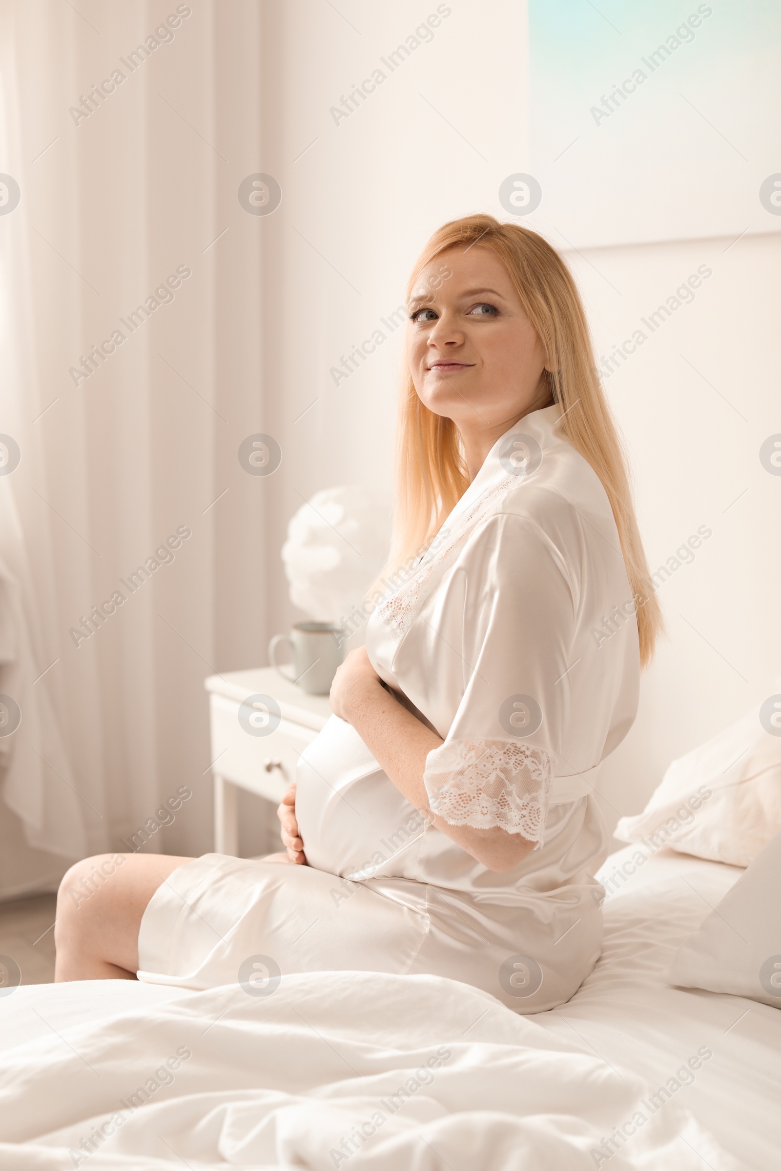 Photo of Beautiful pregnant woman sitting on bed in light room