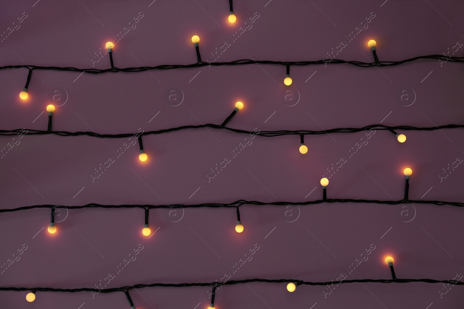 Photo of Glowing Christmas lights on violet background, top view