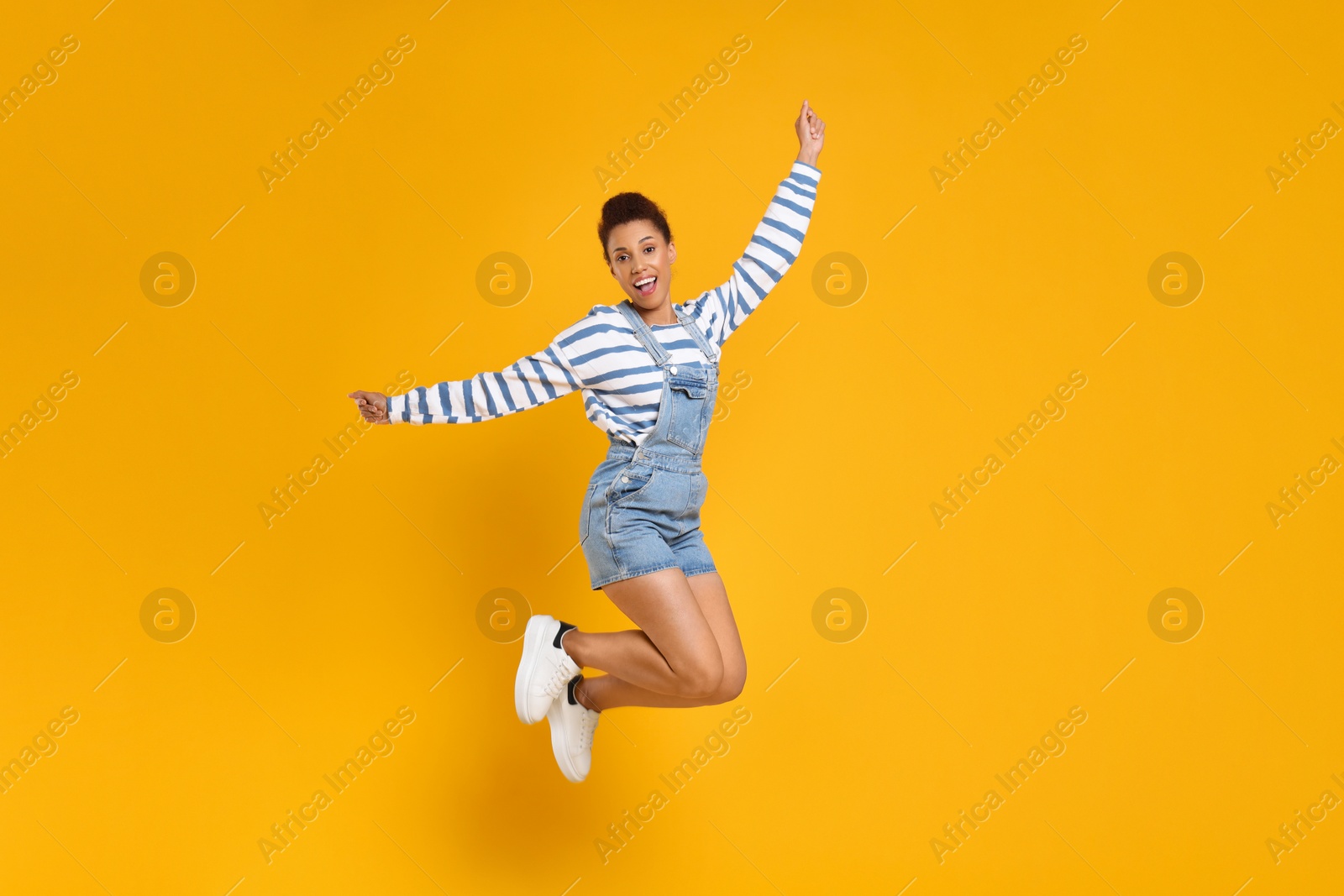 Photo of Happy young woman jumping while dancing on orange background