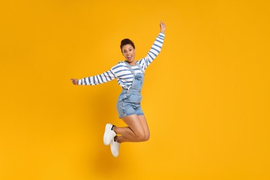 Photo of Happy young woman jumping while dancing on orange background