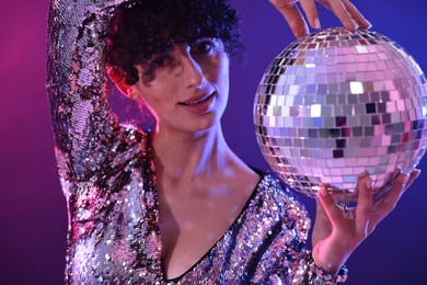 Beautiful young woman with disco ball posing on color background in neon lights, closeup