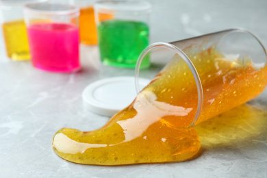 Overturned plastic container with orange slime on marble background, closeup