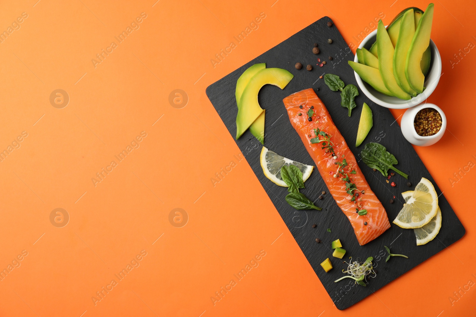 Photo of Delicious salmon with spinach, lemon and avocado on orange background, flat lay. Space for text