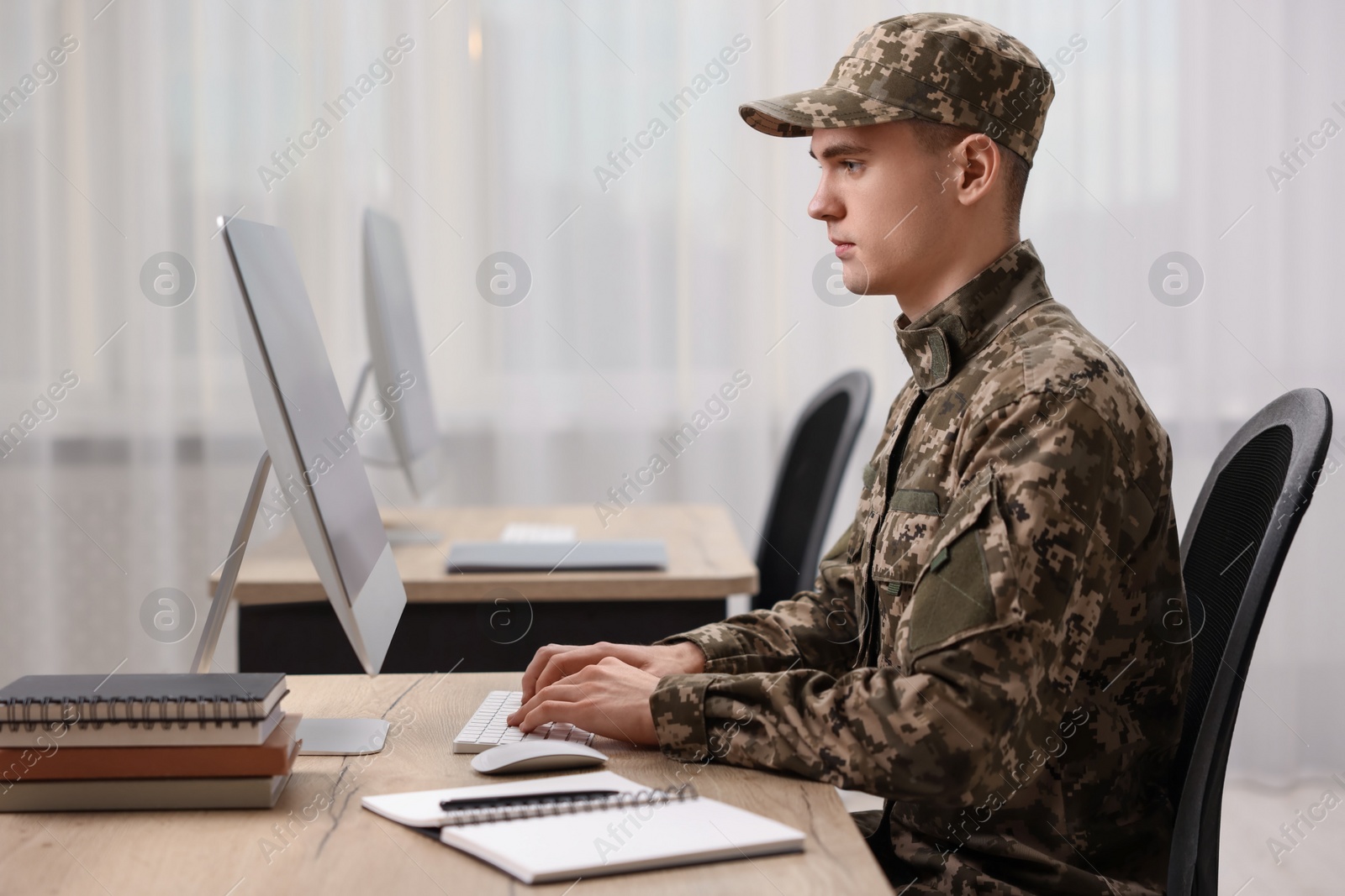 Photo of Military service. Young soldier working with computer at wooden table in office