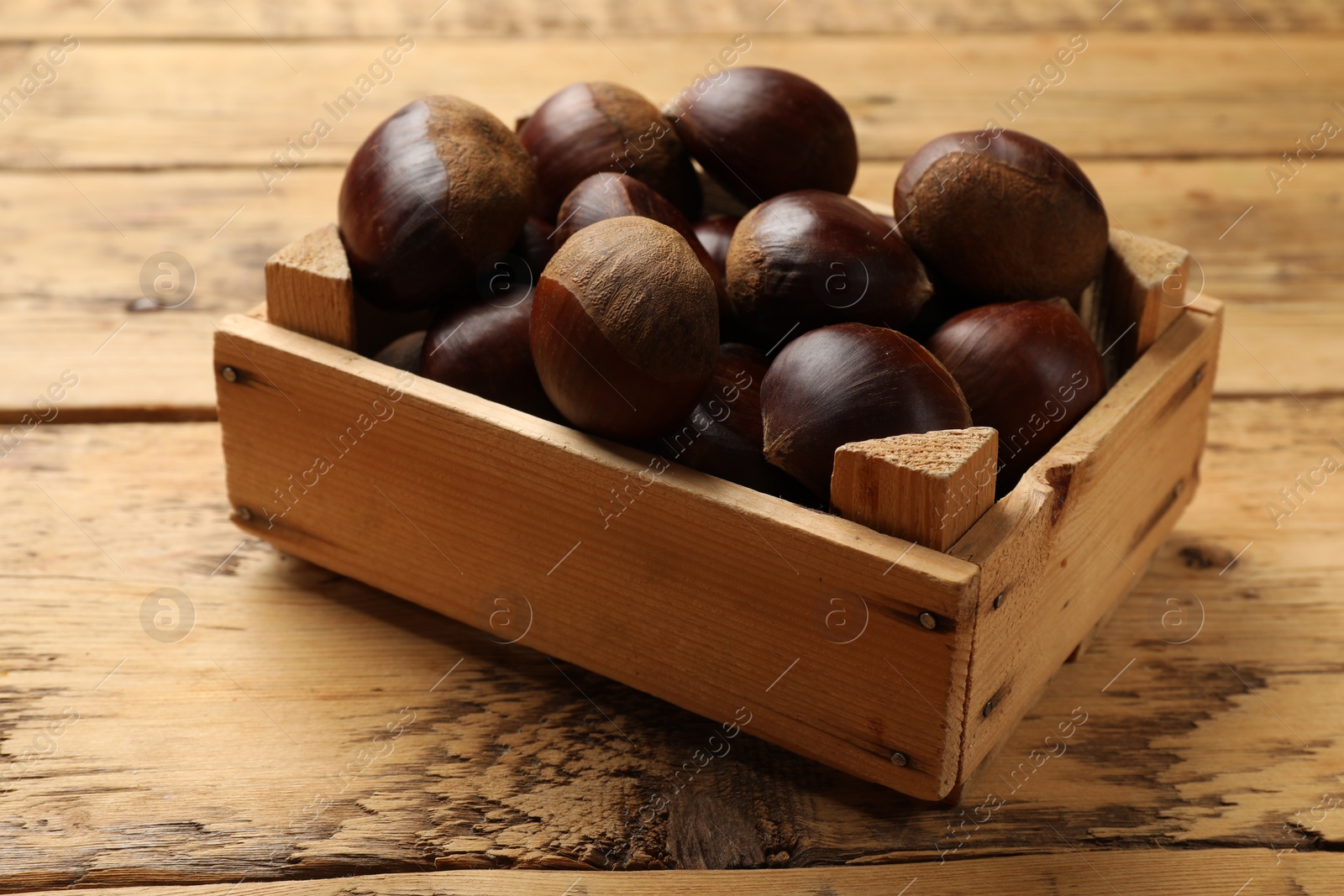 Photo of Sweet fresh edible chestnuts in crate on wooden table