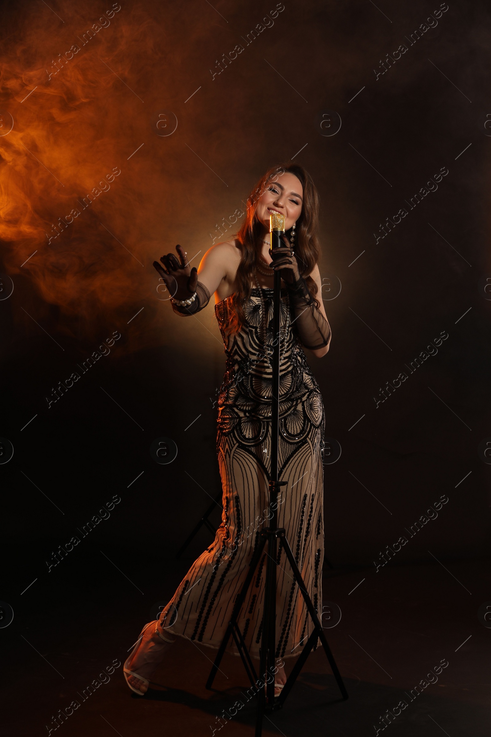 Photo of Beautiful young woman with microphone singing in color lights and smoke