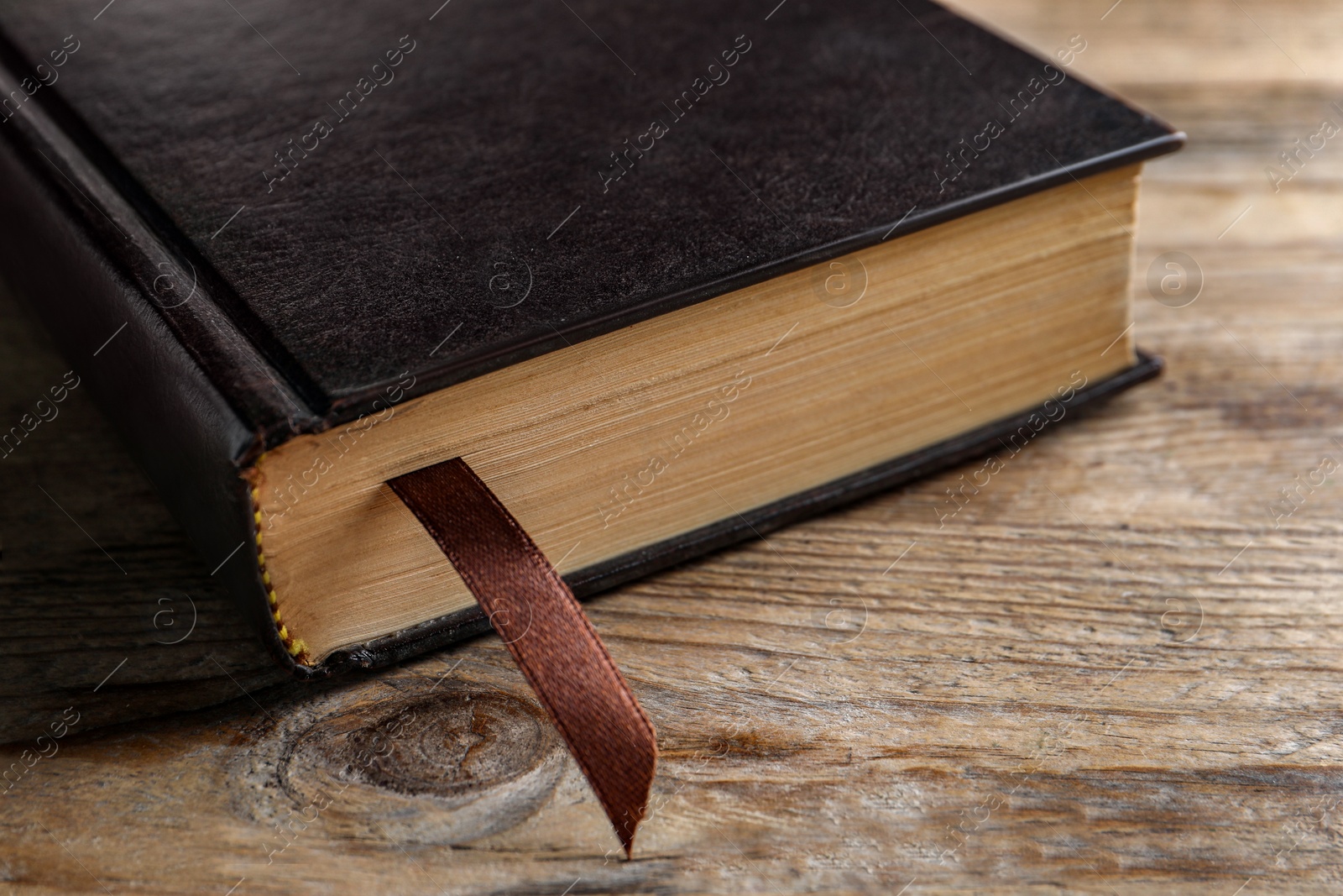 Photo of Bible with dark cover on wooden table, closeup. Christian religious book