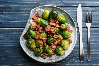 Photo of Tasty roasted Brussels sprouts with bacon on blue wooden table, flat lay