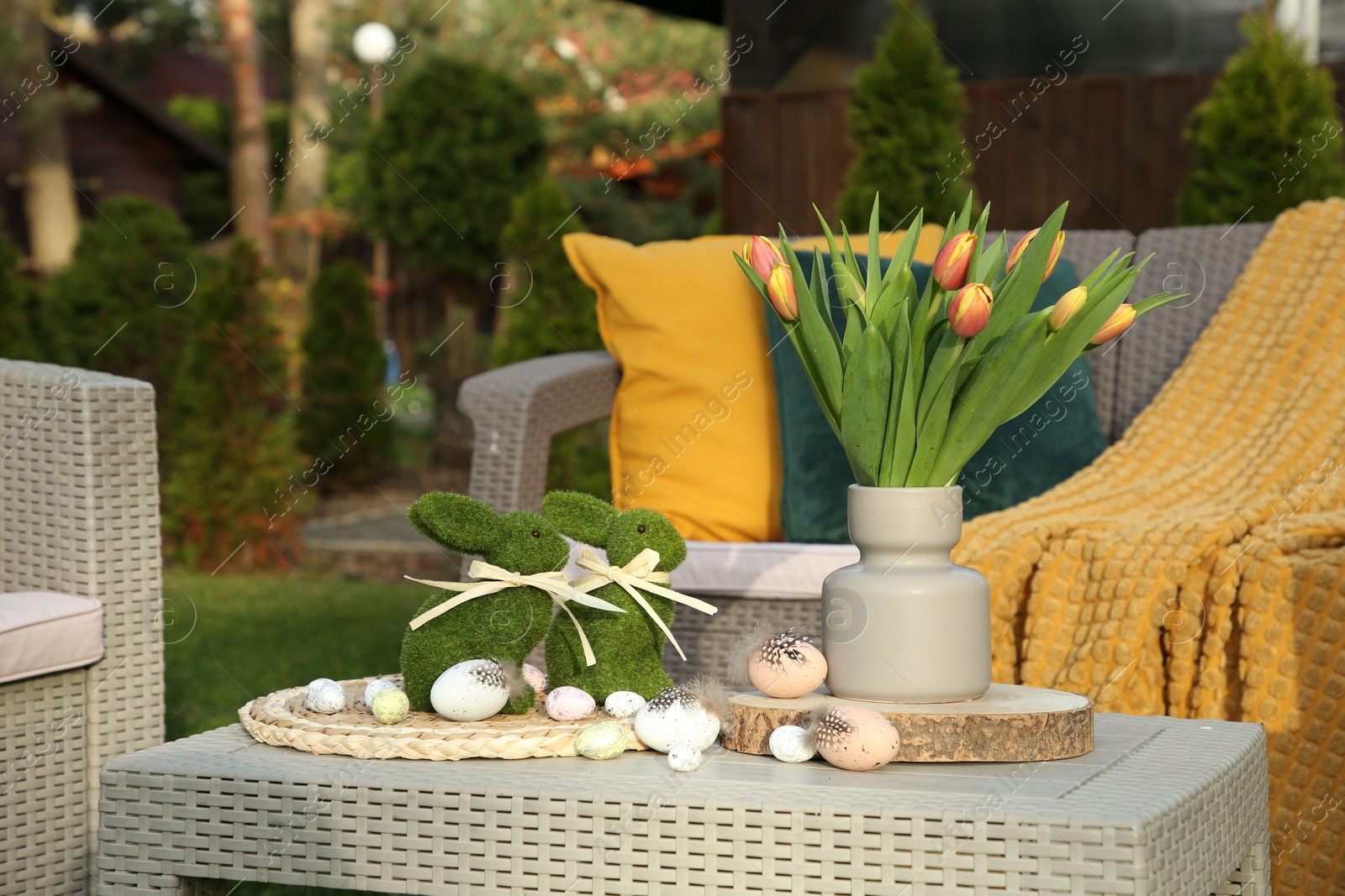 Photo of Terrace with Easter decorations. Bouquet of tulips in vase, bunny figures and decorative eggs on table outdoors