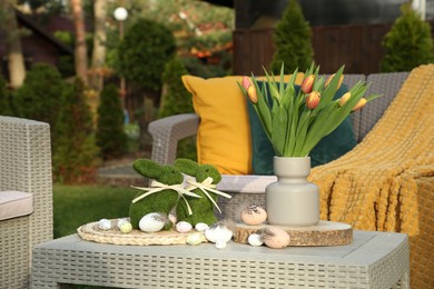 Terrace with Easter decorations. Bouquet of tulips in vase, bunny figures and decorative eggs on table outdoors