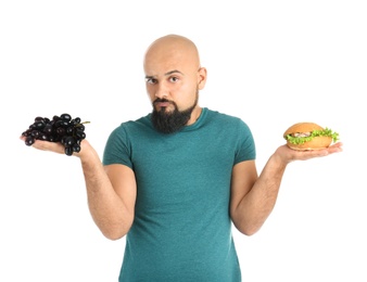 Overweight man with hamburger and grapes on white background