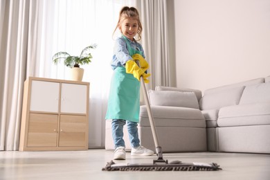 Photo of Little girl mopping floor in living room at home