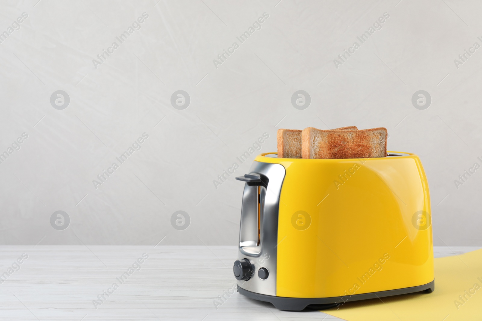 Photo of Modern toaster with slices of bread on white wooden table. Space for text