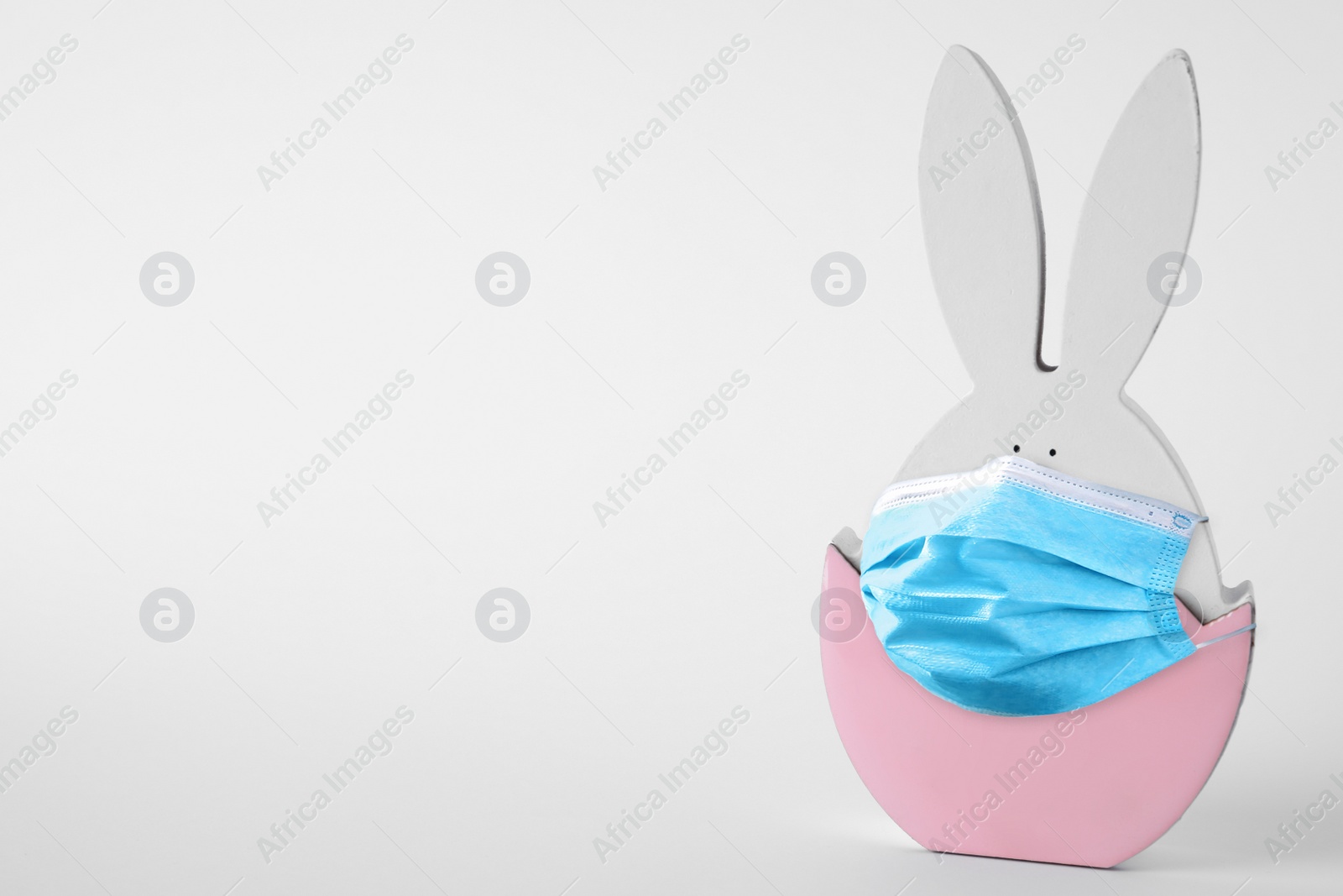 Image of COVID-19 pandemic. Easter bunny figure in protective mask on light background, space for text