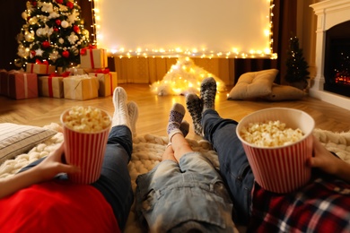 Photo of Family with popcorn watching movie on projection screen in room decorated for Christmas, closeup. Home TV equipment