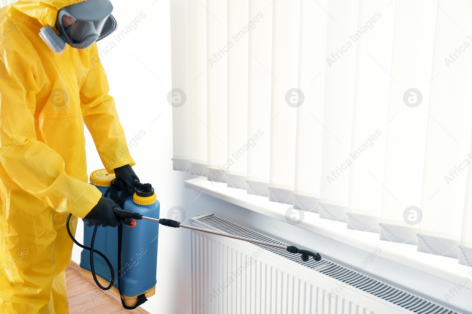 Photo of Pest control worker in protective suit spraying pesticide indoors. Space for text