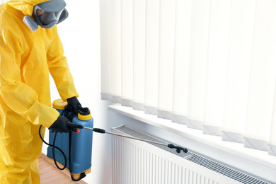 Photo of Pest control worker in protective suit spraying pesticide indoors. Space for text