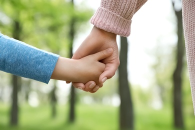Photo of Little child holding hands with his mother outdoors, closeup. Family time