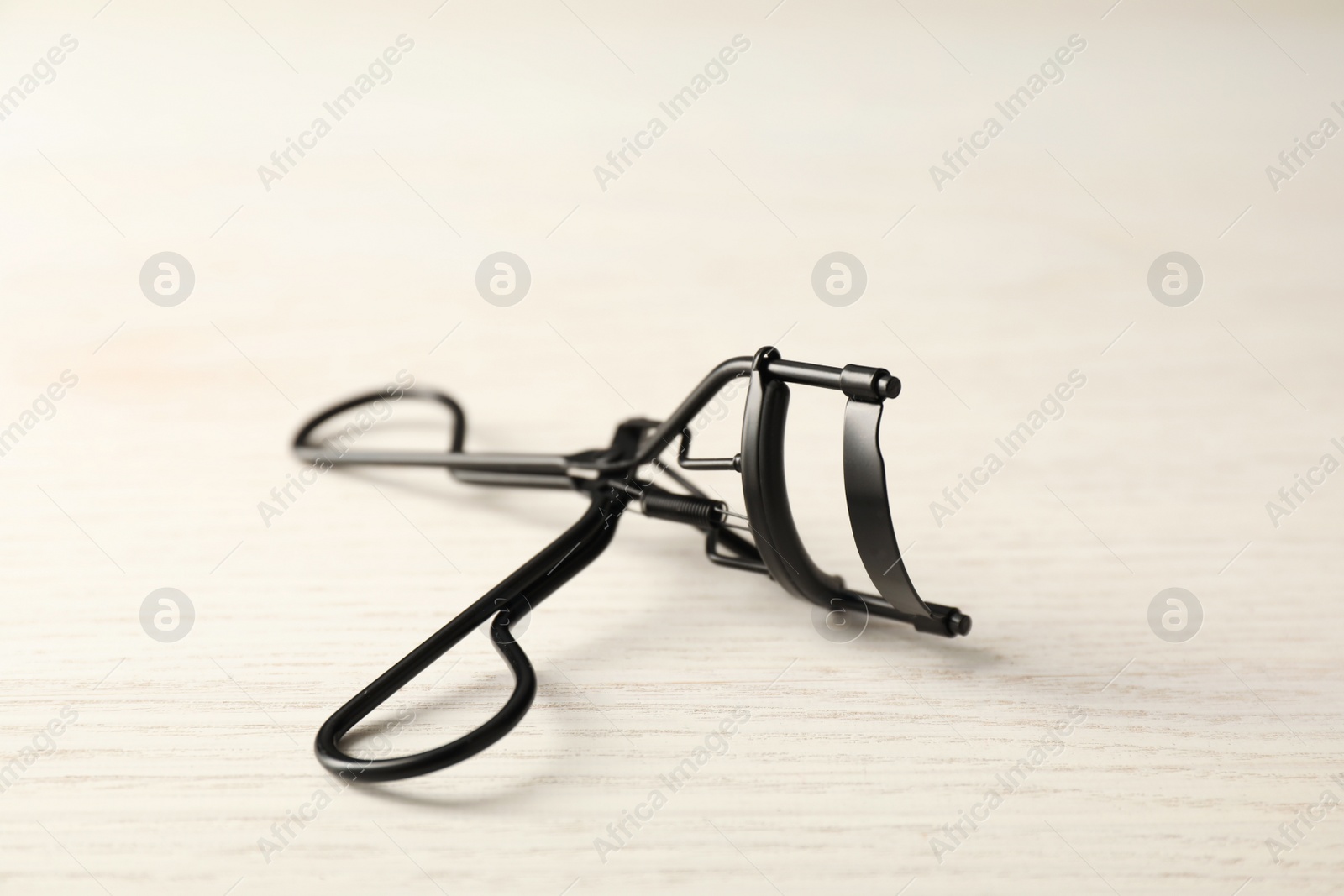 Photo of Eyelash curler on white wooden table, closeup. Makeup tool