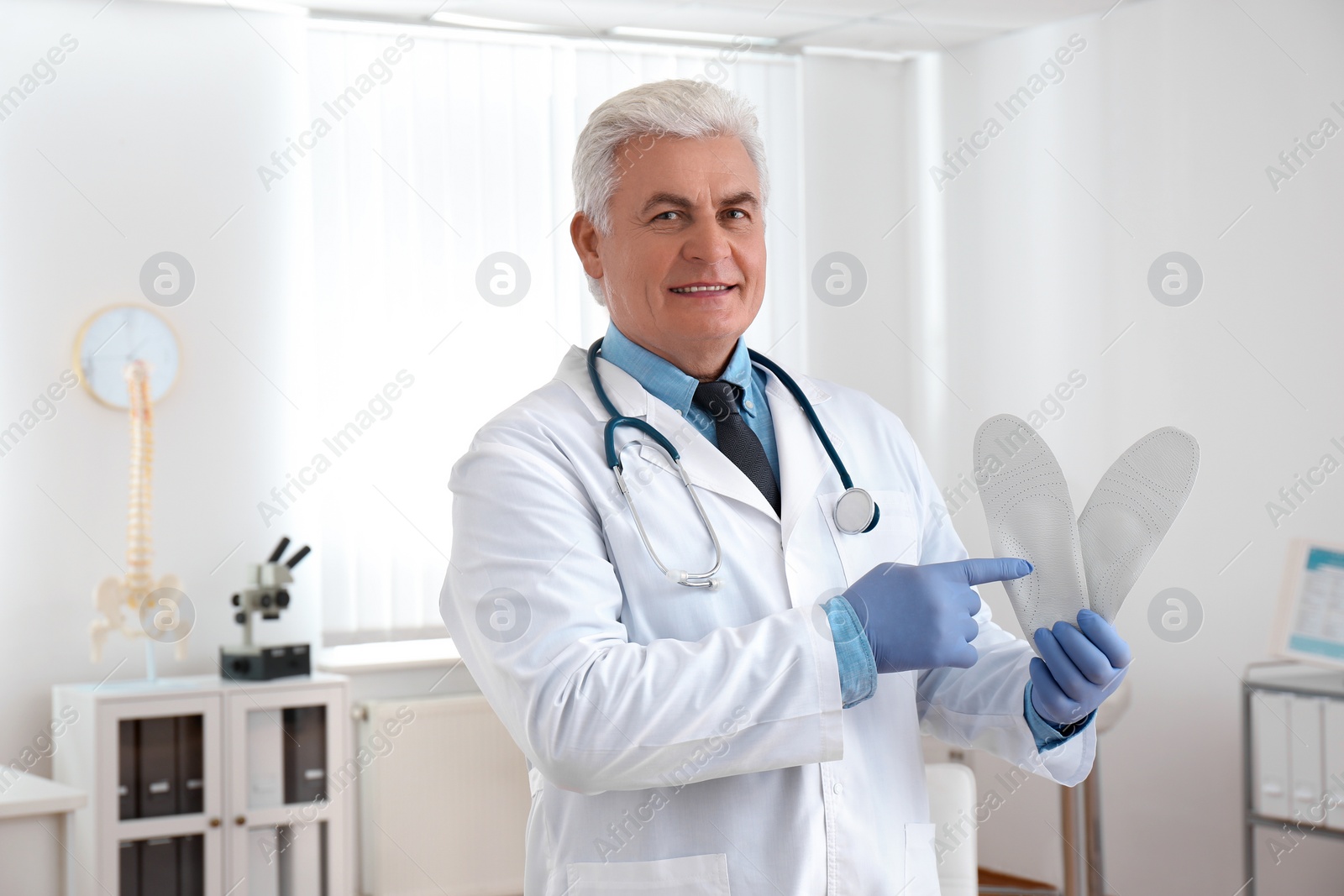 Photo of Senior male orthopedist showing insoles in clinic