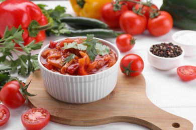 Delicious lecho in bowl and fresh ingredients on white wooden table