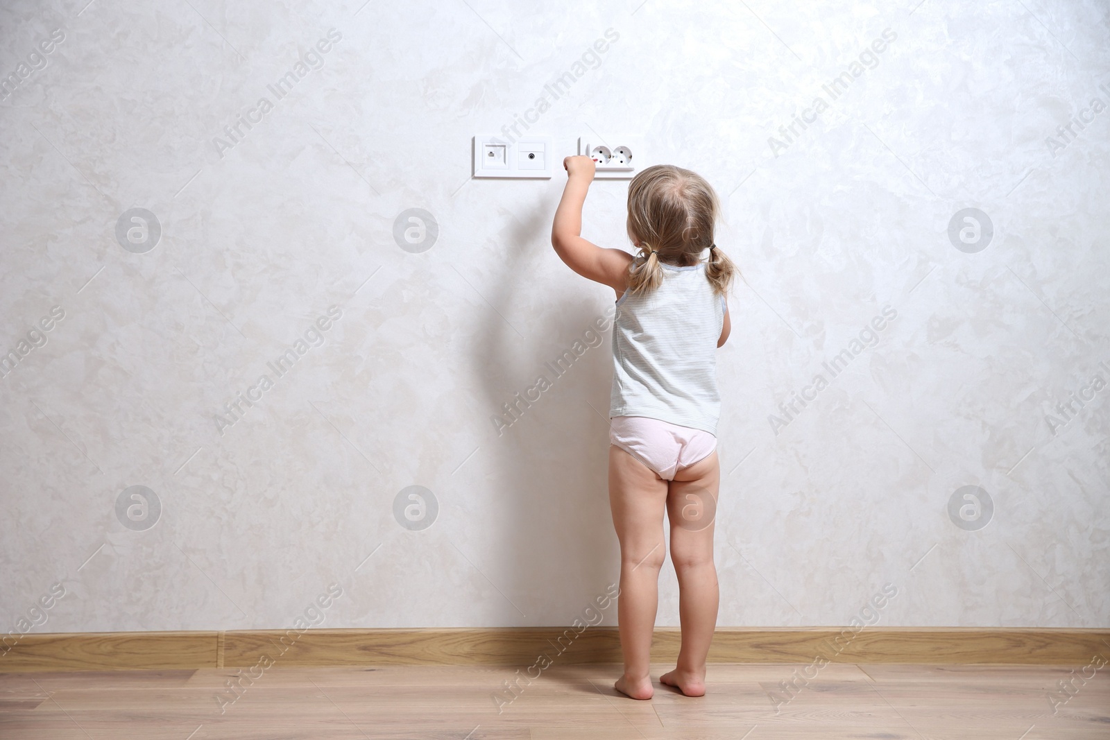 Photo of Little child playing with electrical socket indoors, back view. Dangerous situation