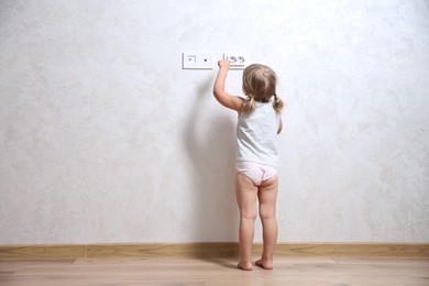Little child playing with electrical socket indoors, back view. Dangerous situation