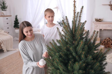 Happy mother with her cute son decorating Christmas tree together at home