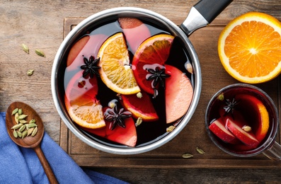 Photo of Delicious mulled wine and ingredients on wooden table, flat lay
