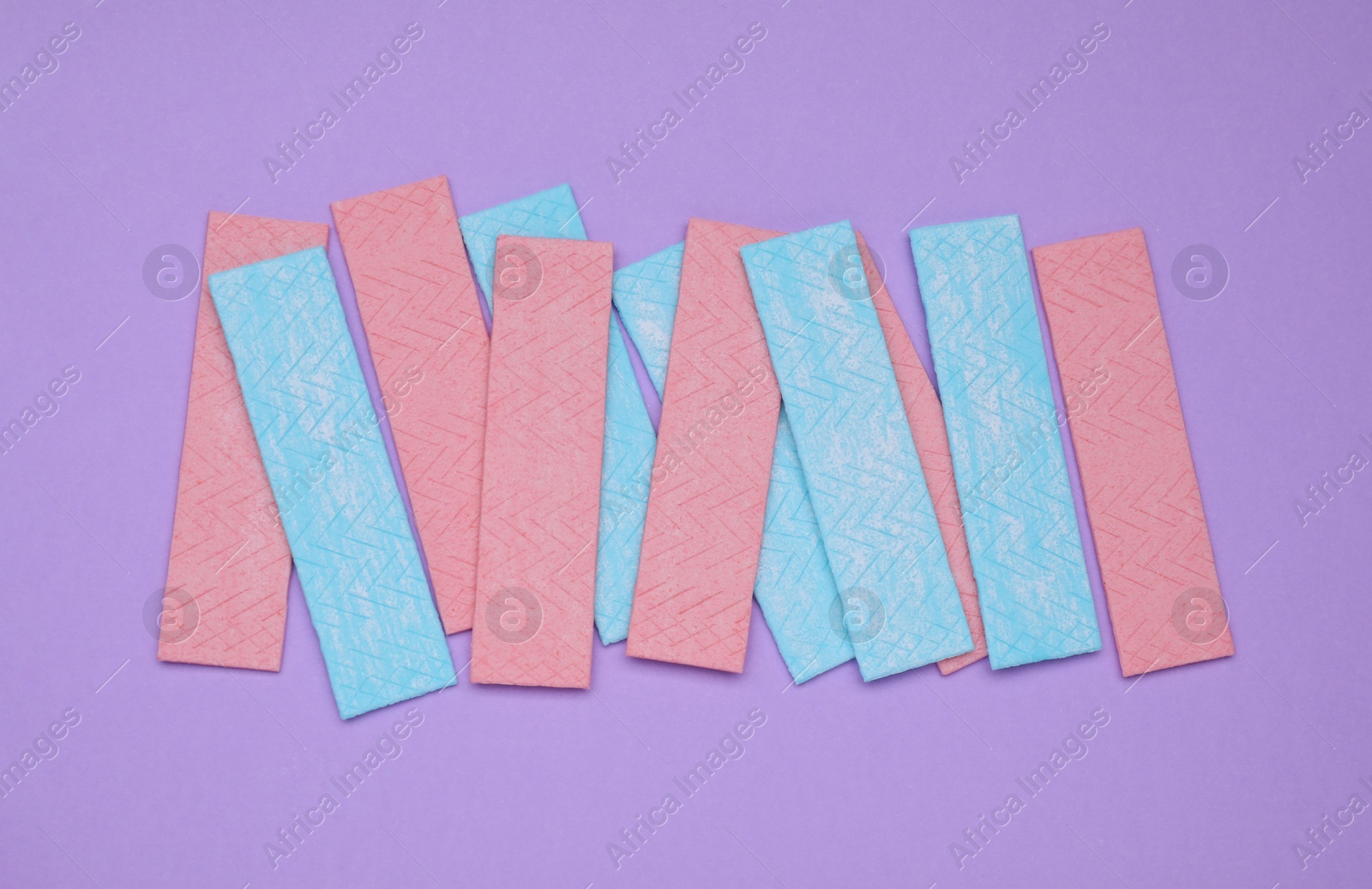 Photo of Many sticks of tasty chewing gum on violet background, flat lay