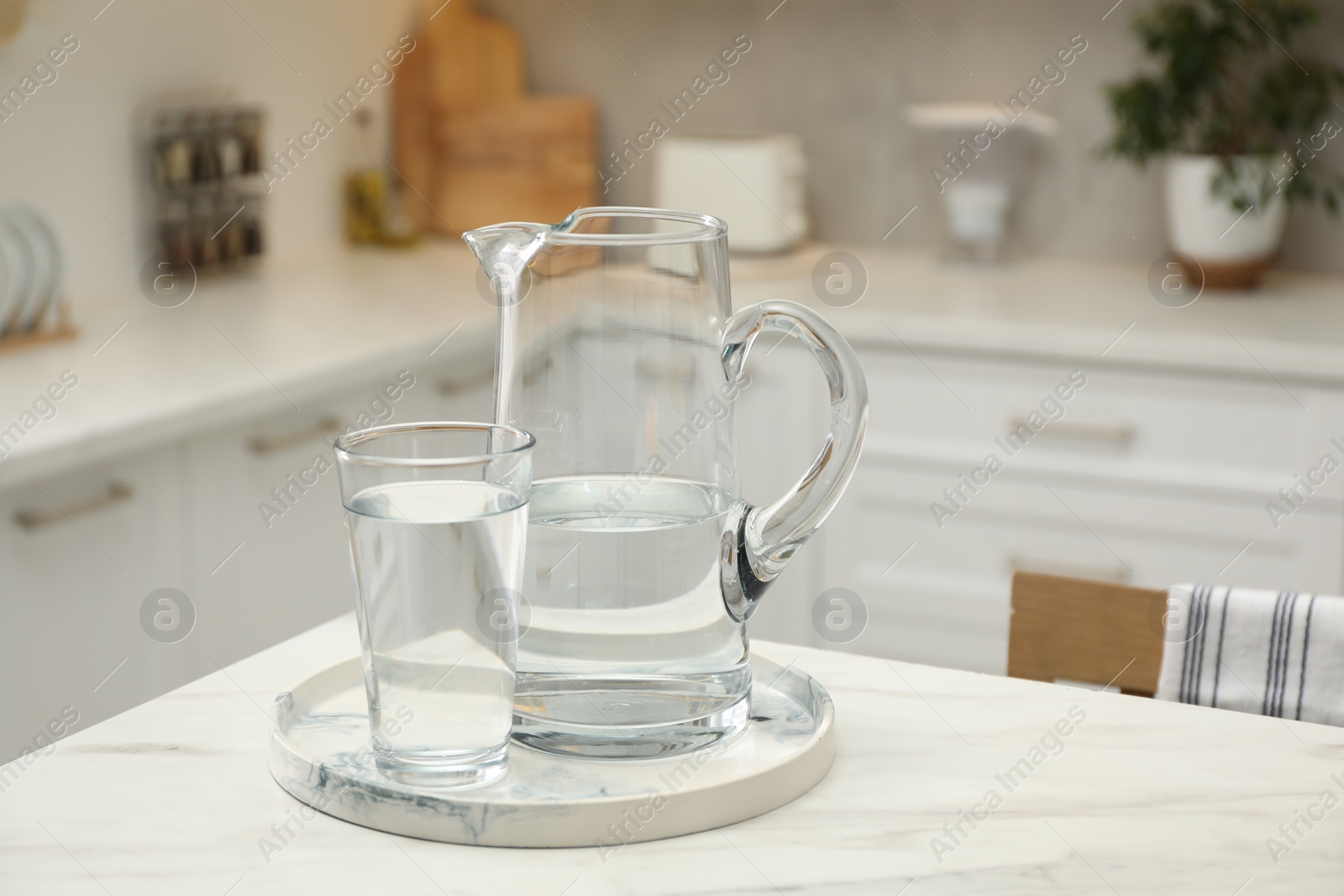 Photo of Jug and glass with clear water on white table in kitchen