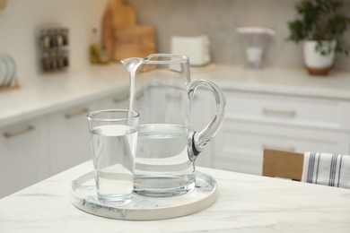 Photo of Jug and glass with clear water on white table in kitchen