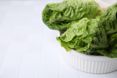 Photo of Bowl with fresh green romaine lettuces on white tiled table, closeup. Space for text