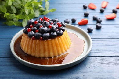 Photo of Delicious pudding with caramel and berries on blue wooden table