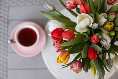 Beautiful bouquet of colorful tulips and cup with drink on grey table, top view. Space for text