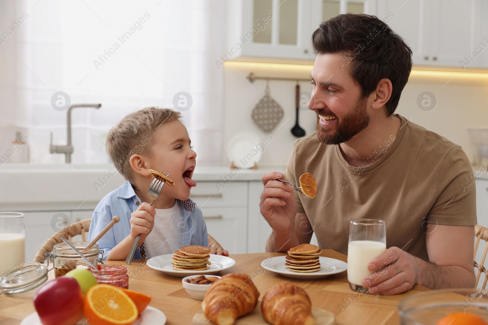 Photo of Father and his cute little son having breakfast at table in kitchen