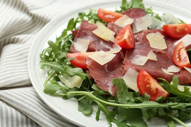 Photo of Delicious bresaola salad with parmesan cheese on tablecloth, closeup view
